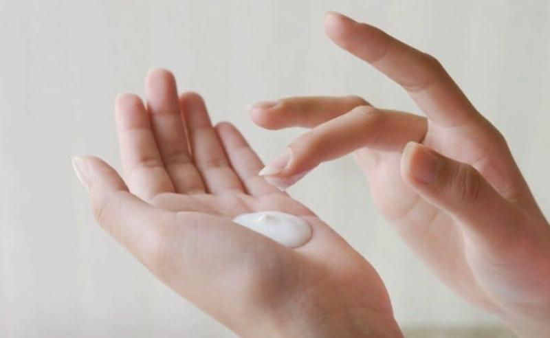 Một bàn tay đang đong lượng kem chống nắng Aqua Nhật (dạng sữa hoặc gel lỏng) bằng cách vạch lên hai ngón tay trỏ và giữa, minh họa cho lượng dùng chuẩn 2 đốt ngón tay.